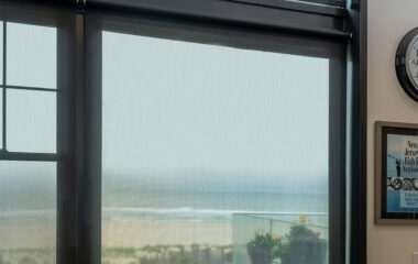 A sea view though a window fitted with automated shades.